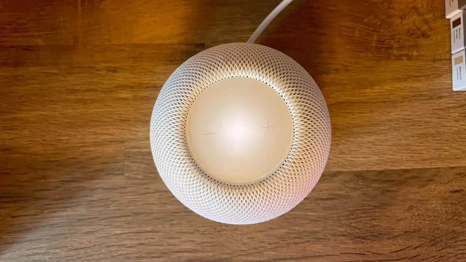 A white HomePod mini on a wooden surface with the touch panel illuminated