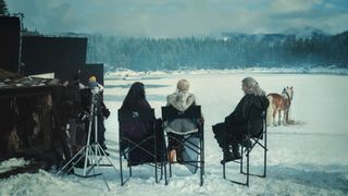 Behind-the-scenes shot from The Witcher season 3 which shows Henry Cavill, Freya Allan and Anya Chalotra sitting down facing away from the camera in a snowy landscape