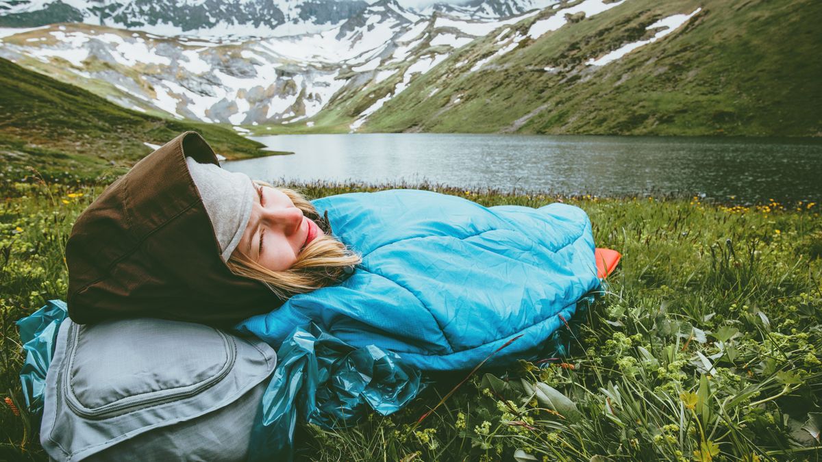 A woman in a blue bivy sack by an alpine lake