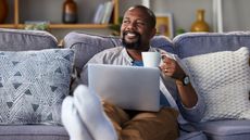 A man with a cup of coffee and his laptop on his lap on the sofa looks relaxed.