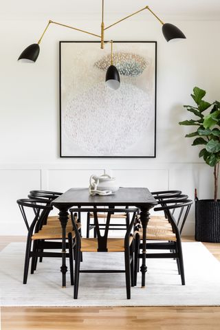 dining table with black table and chairs, large artwork, pendant with 3 black shades, brass