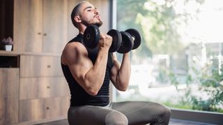Man performing a seated press at home with dumbbells curled below his chin