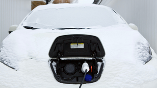 An electric car being charged on a snowy winter day. 
