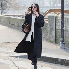 she wears white button down, coat, black pants and shoes while holding a handbag tucked under her arm