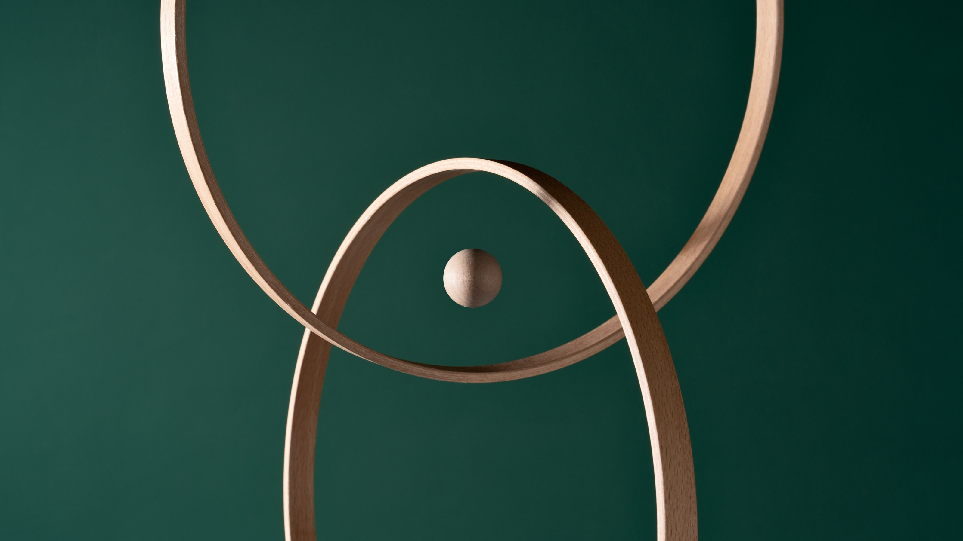 A wooden sphere in the center of intersecting rings against a green background.
