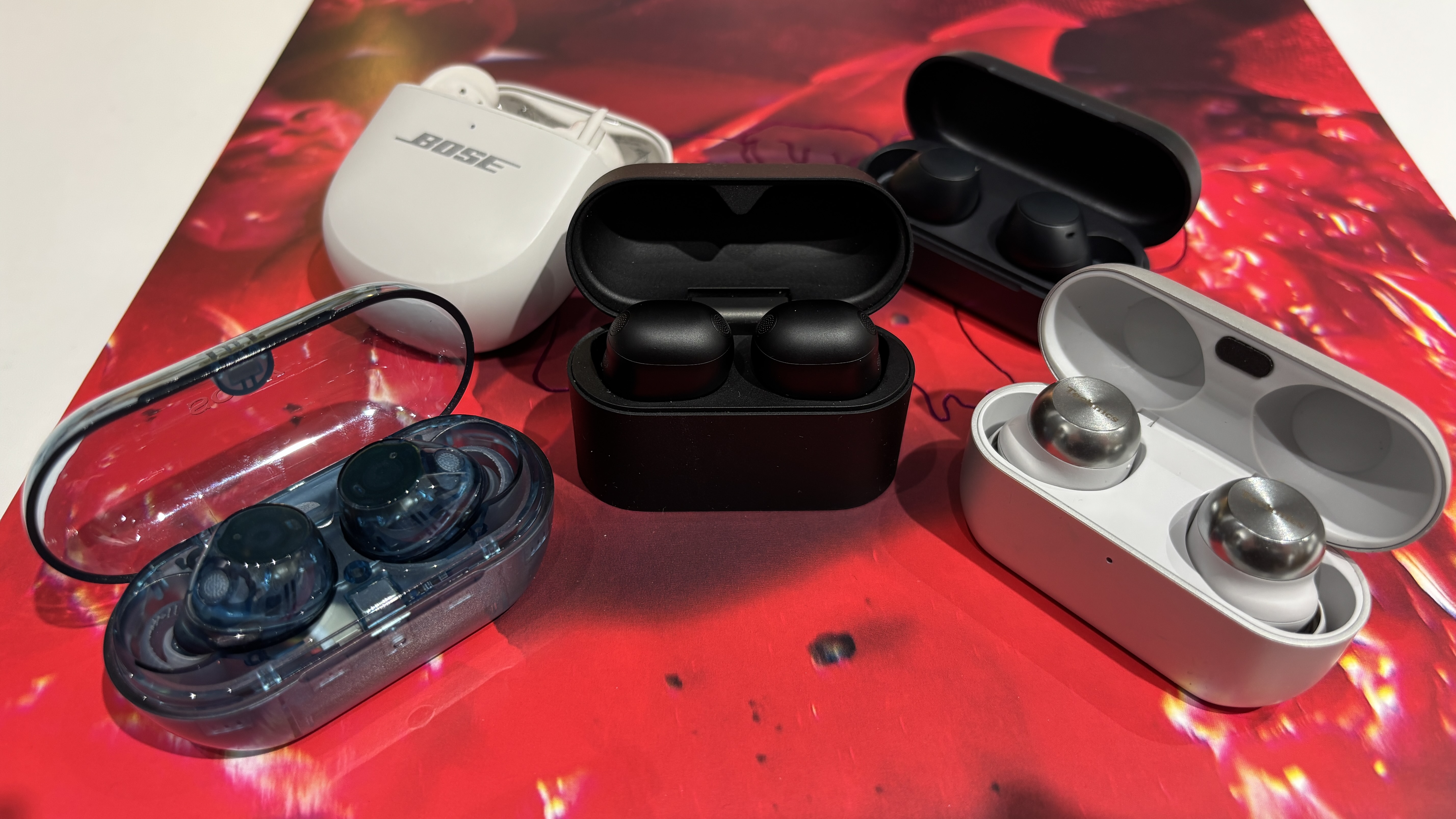 A selection of wireless earbuds with their cases opened places on a red record cover