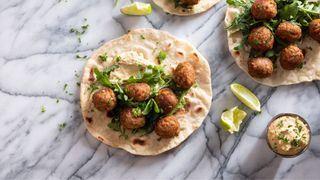 Vegan foods sitting on wrap breads with hummus and green vegetables and lime