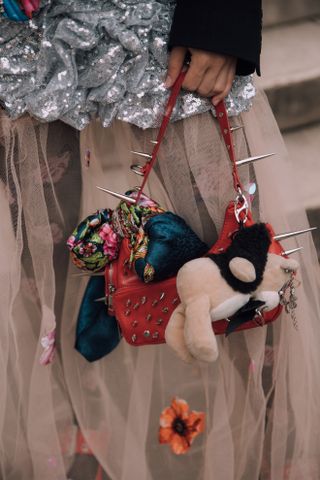 a close up of a woman at fashion week carrying a spiky bag with a stuffed animal attached to it