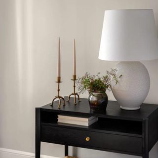 A black nightstand with a white table lamp and candles