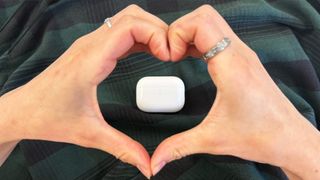 a photograph of an airpods pro 2 case on a green background with heart hands