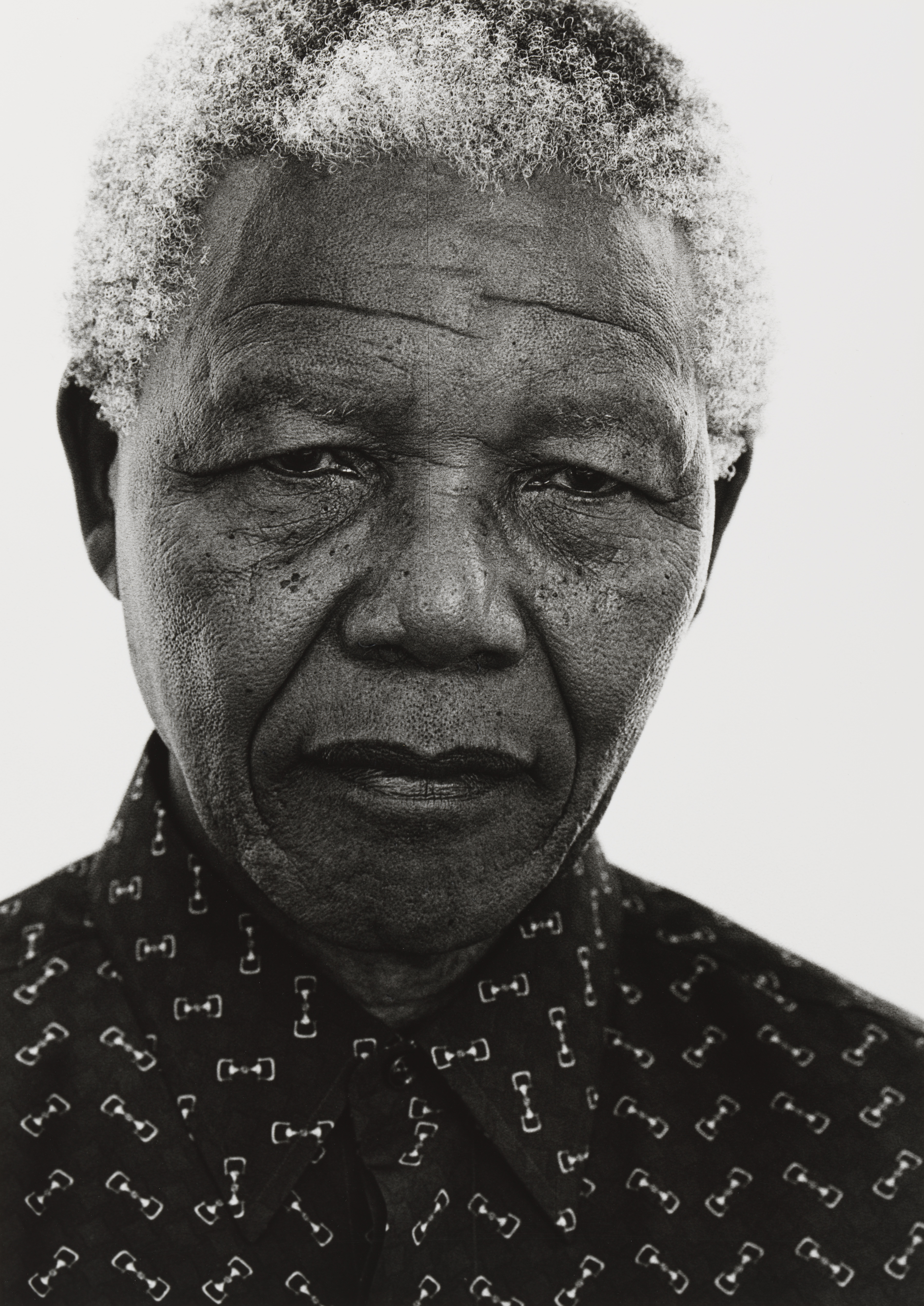 Jillian Edelstein's close black-and-white portrait of Nelson Mandela, his gaze slightly downcast and expression reflective, wearing a patterned shirt against a plain background.