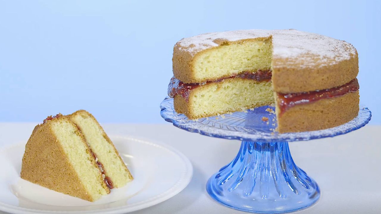 Mary Berry&#039;s Victoria sponge on a cake stand with a slice cut out and served on a plate