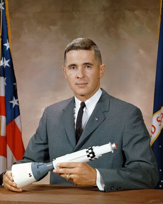 a man in a gray suit holds a model of a rocket