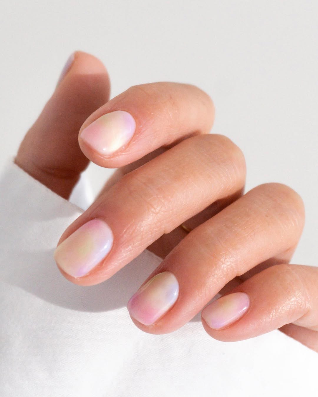 a diffused white polish on nails with subtle pops of yellow pink and blue