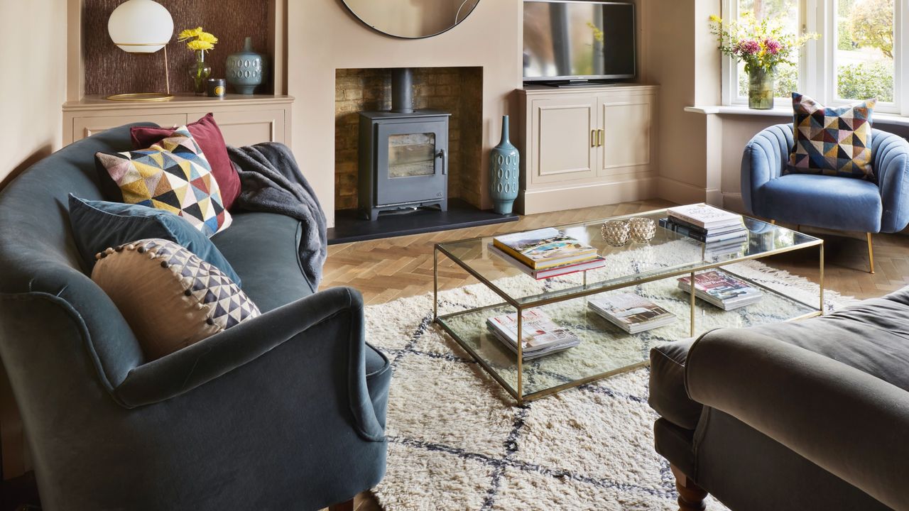 A peach-painted living room with a blue velvet sofa and chair decorated with patterned cushions and a throw