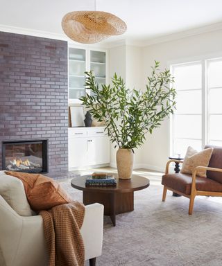 A living room painted white with a red brick fireplace and a large plant on a coffee table