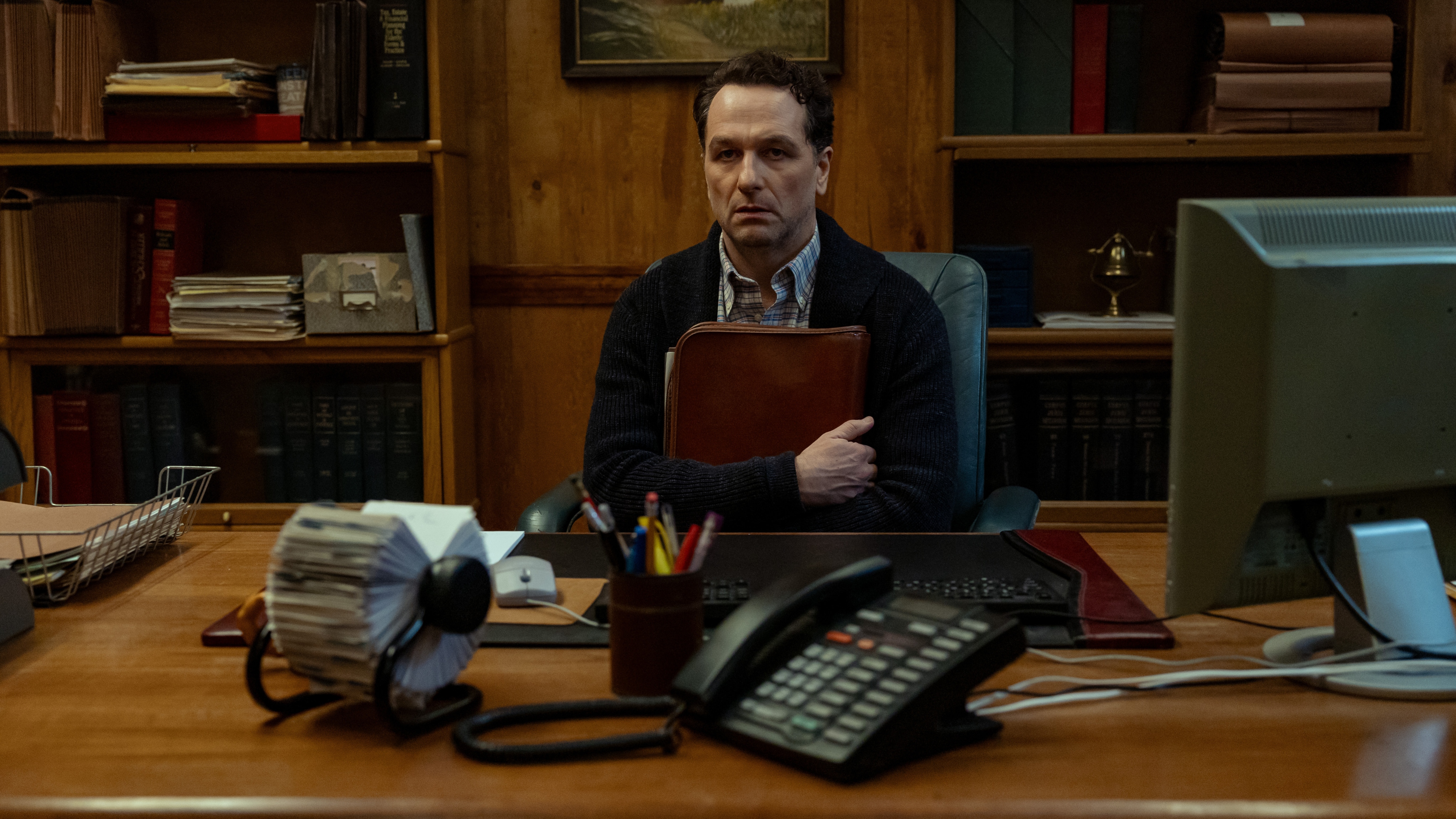 Matthew Rhys as Mayor Tom Loftis looking shaken as he hugs a briefcase while sitting in an office.