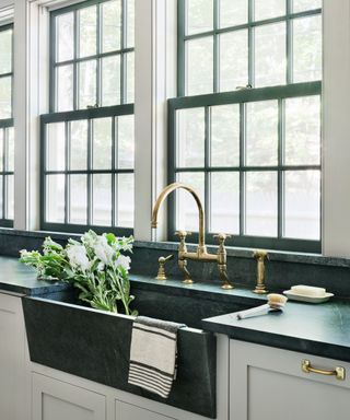 An off-white kitchen with black soapstone countertops and sink basin with a gold faucet