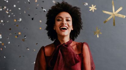 Woman wearing a party dress and one of the best christmas hairstyles - bouncy curls, on a grey backdrop with glitter