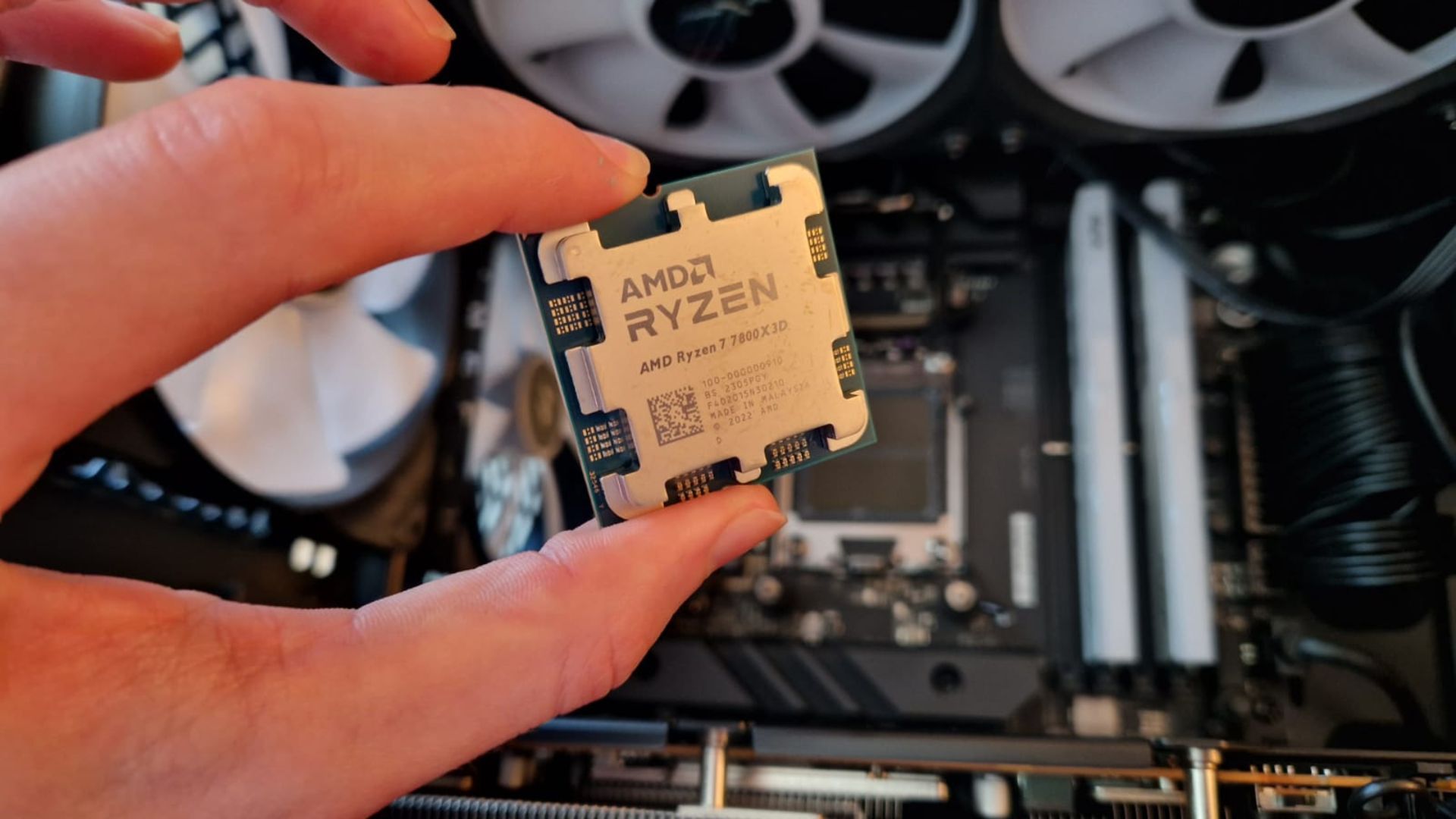 An AMD Ryzen 7 7800X3D review image showing the CPU being held above a motherboard