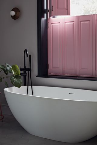 Bright pink shutters in small bathroom with freestanding bath