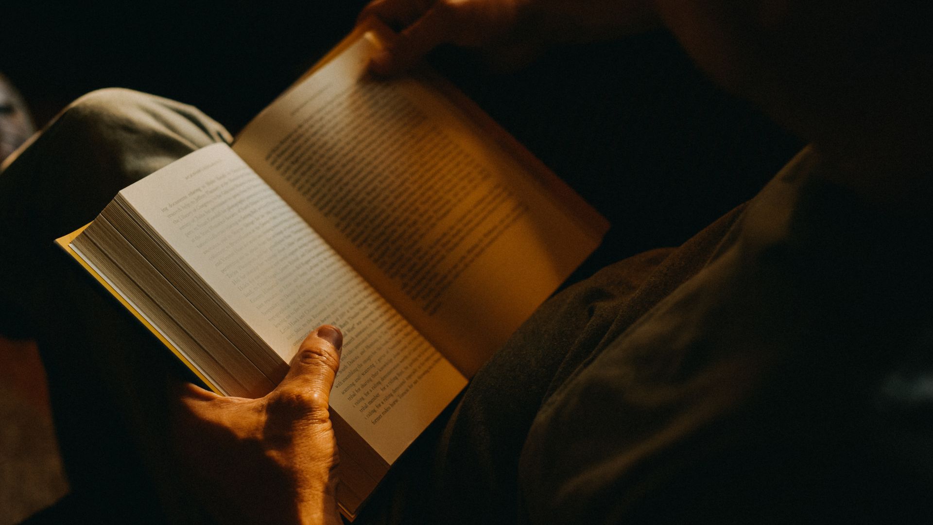 A person reading a book in a dimly-lit room.