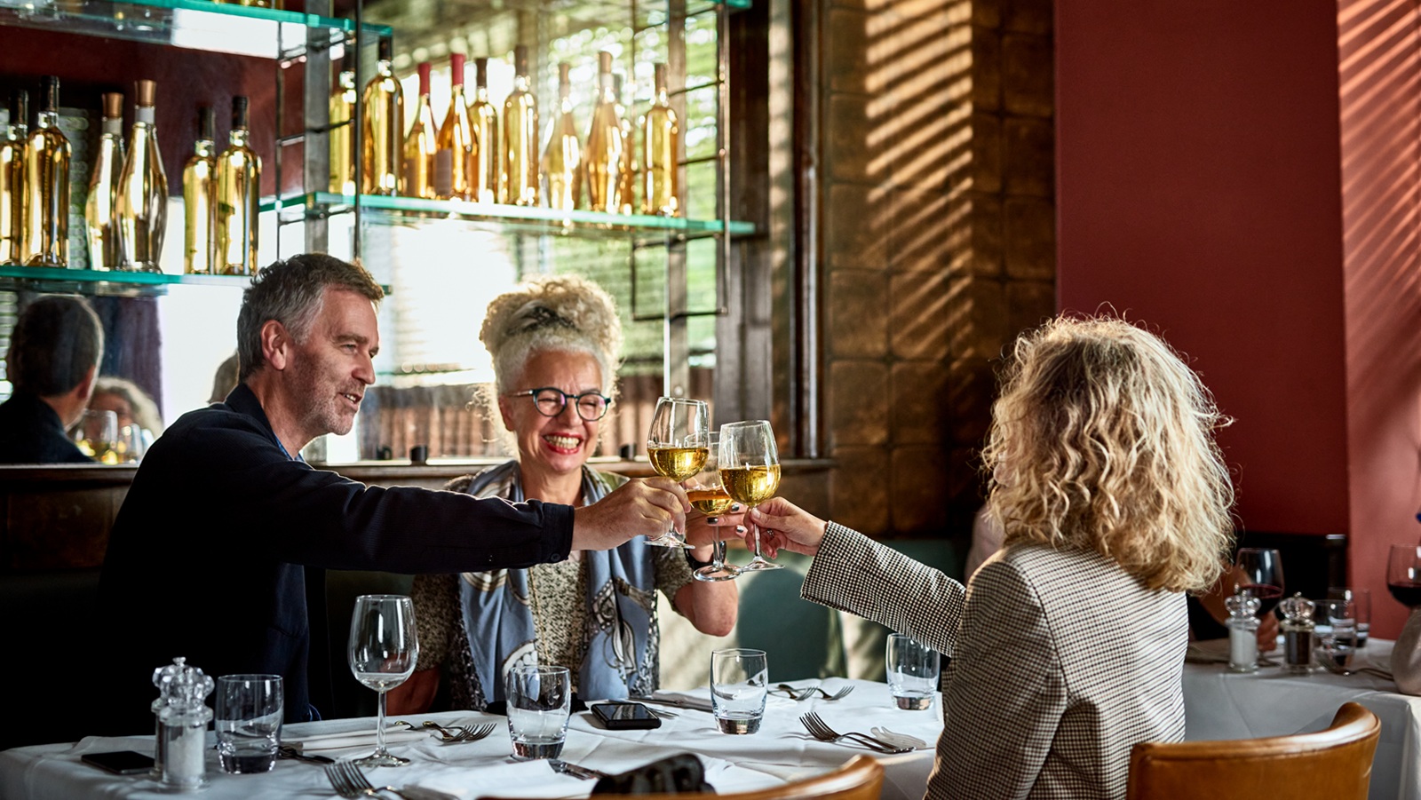 Senior woman and mature couple celebrating over dinner with white wine, smiling, happiness, good news