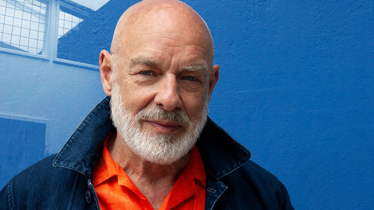 Brian Eno portrait against a blue wall, 2022