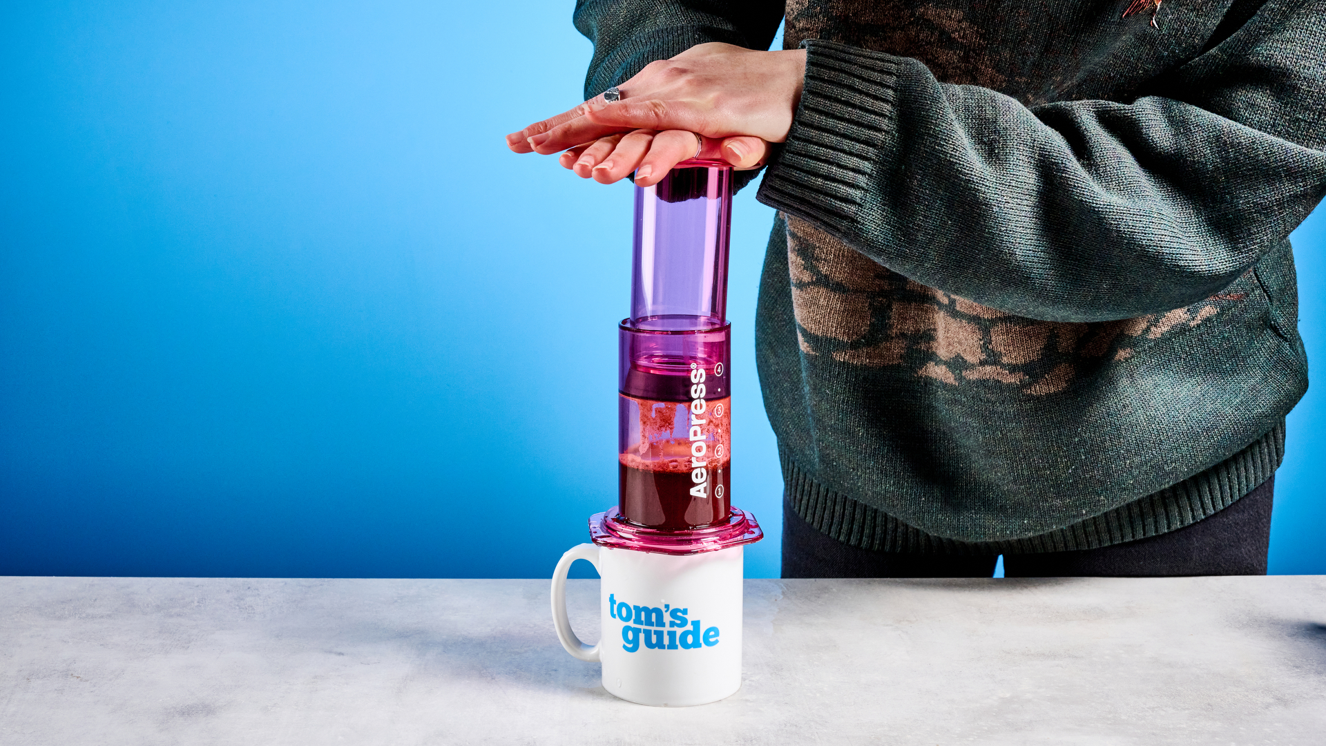 the aeropress clear color in pink photographed against the blue tom's guide background