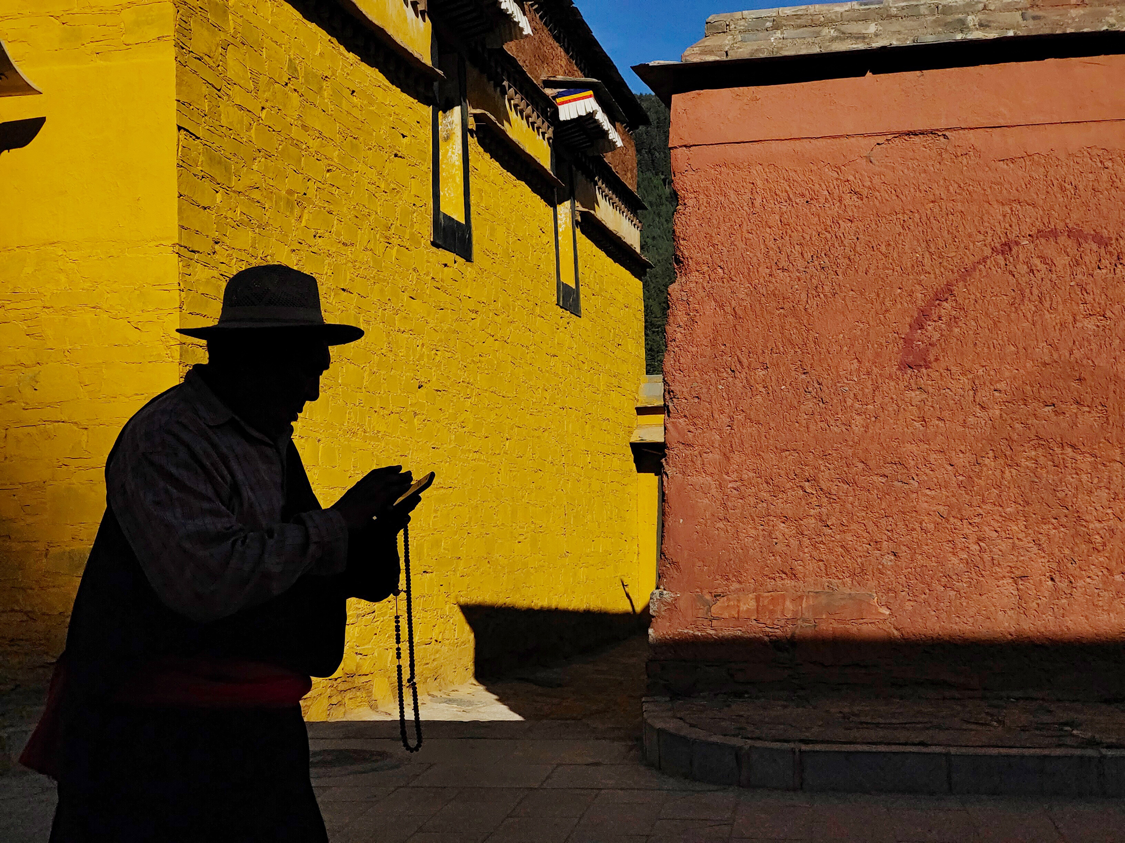 A silhouette of a person holding prayer beads walks past vibrant yellow and orange walls, casting long shadows