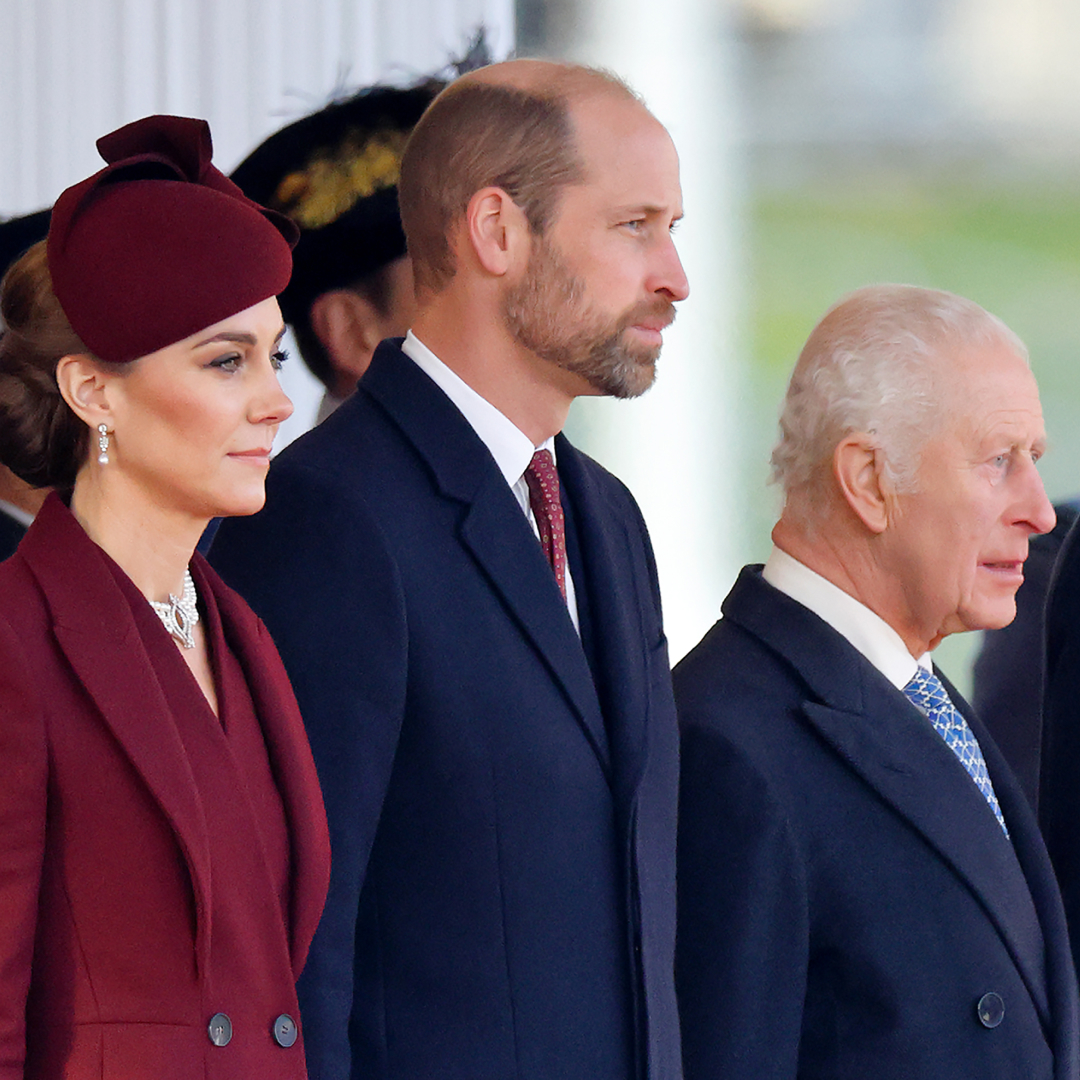 Kate Middleton wears a burgundy coat and matching hat, Prince William wears a navy coat and red tie, and King Charles wears a navy coat with a white shirt and blue tie