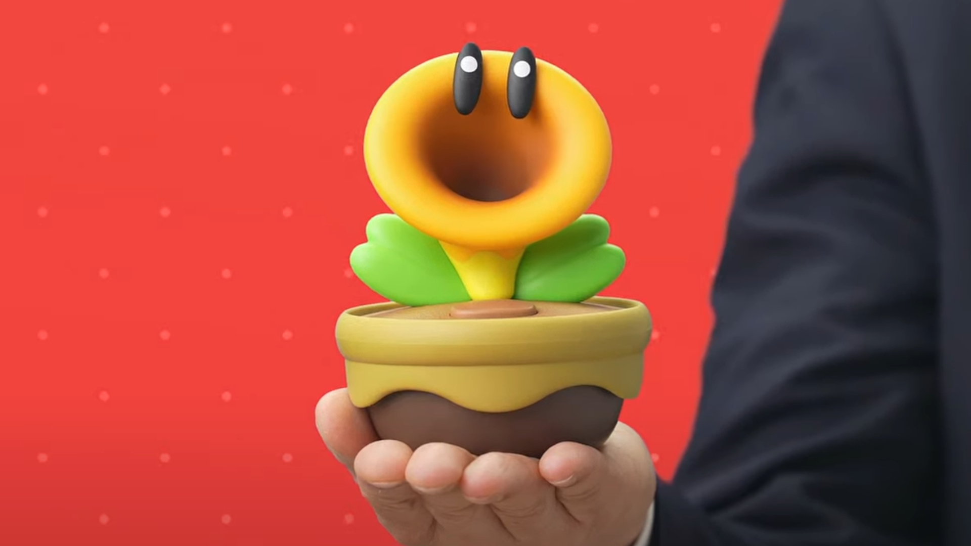 A hand holds the Talking Flower replica from Super Mario Wonder against a red background