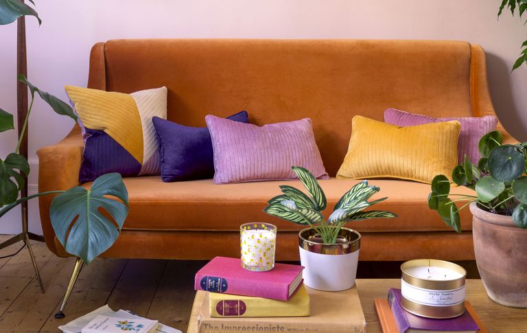 orange sofa in a colourful living room with multi coloured cushions and books and plants on a coffee table