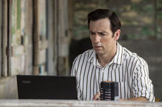 Death In Paradise season 13 episode 4: Neville (Ralf Little) sits at his laptop on the veranda of his beach house, looking at the screen with concern