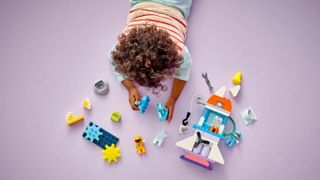 Lego Duplo Space Shuttle Adventure set being played with by a young child on a pink background.