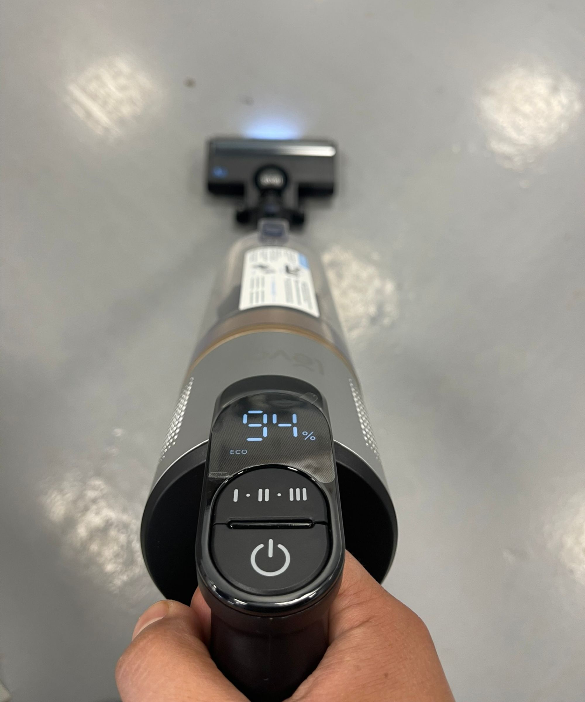 Closeup of the Levoit LVAC-300 cordless vacuum cleaner from above, showing the power button, suction mode button, and screen showing 94 battery life and ECO mode in Future test center.