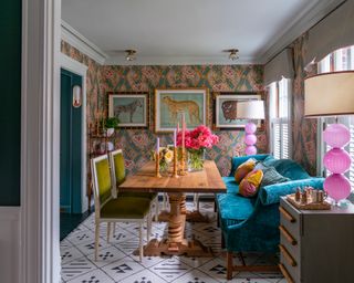 A dining room with teal velvet dining sofa and Gucci patterned wallpaper