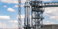 A white and black Blue Origin rocket stands on the launch pad for a suborbital NS-27 launch.