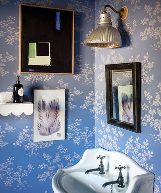 A decorative gold wall lamp over a white sink in a wallpapered powder room