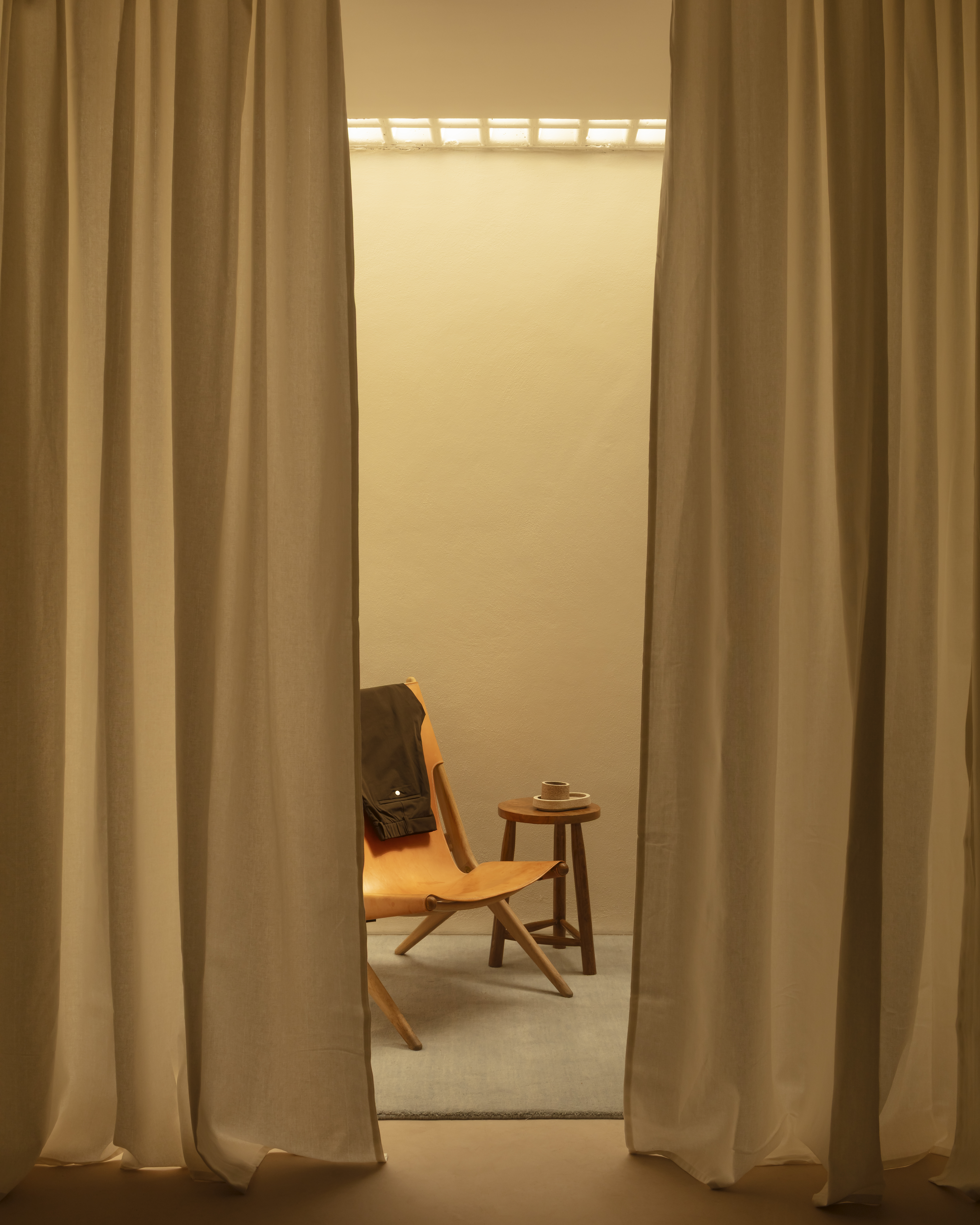 Different corners of a sleek menswear store clad in warm woods, beige drapery, and silver and mint green accents.