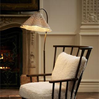 A wooden and boucle armchair next to a scalloped patterned floor lamp