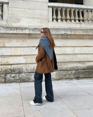 Woman wears brown suede jacket, blue jeans and grey knitted triangle scarf