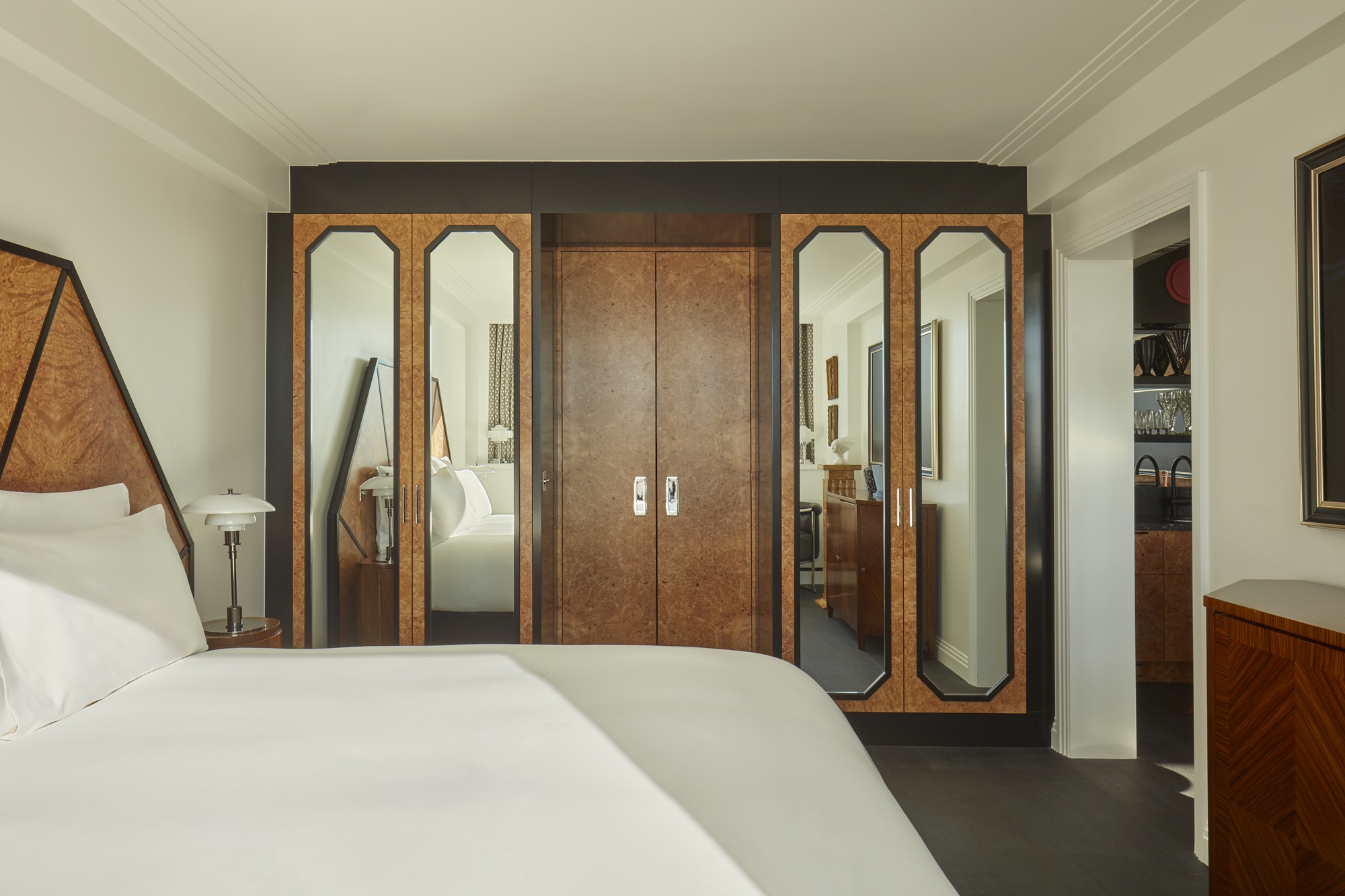 an art deco bedroom with angular burl wood headboard and built ins with angular mirror inserts