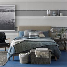 Coastal grey bedroom with striped wallpaper, fitted shelf, framed photograph,double bed, blue and grey bedlinen, vintage sidetable, wicker basket case.