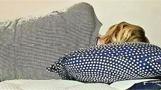 A woman with blonde hair sleeps on a blue pillow on a DreamCloud mattress