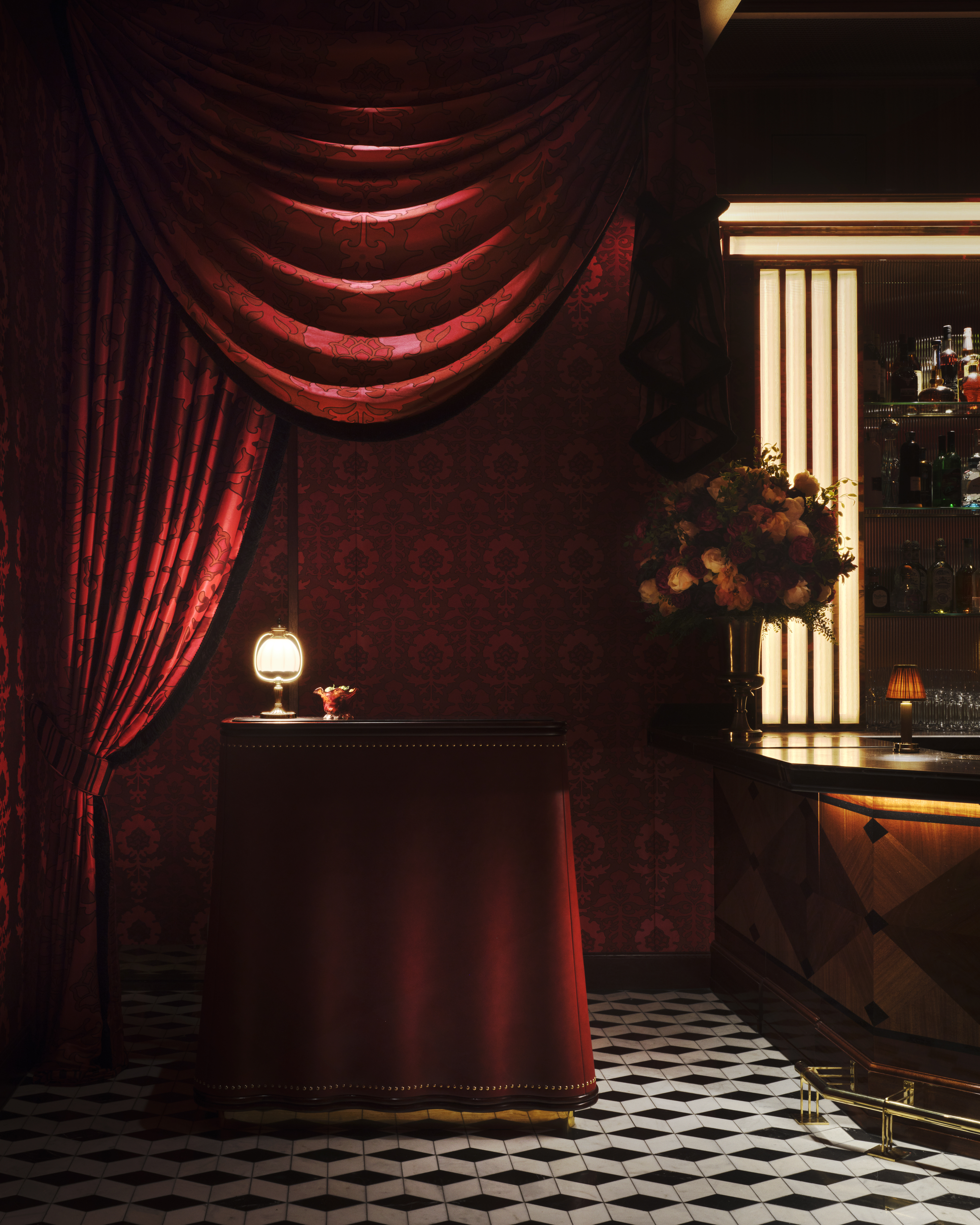 A dazzling decorated restaurant with checkered, red and white marble floors, red velvet drapery, banquettes, and leather chairs, ciambella-shaped lighting with a golden glow, and softly burning table lamps.