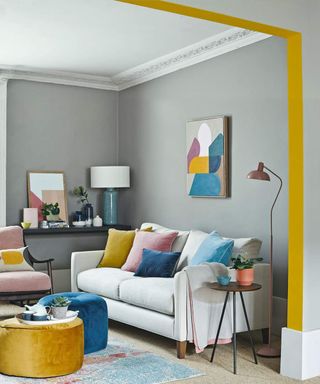 living room with grey walls, yellow painted archway and matching artwork and pastel cushions.