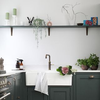 Dark green kitchen cabinets, sink, shelving