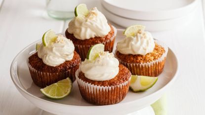 Lime cupcakes on a cake stand surrounded by fresh lime wedges