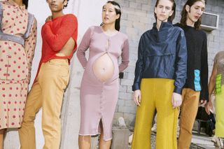 A pregnant woman wearing a clingy ribbed jersey dress, unbuttoned to reveal her bump